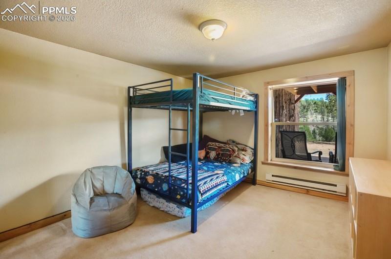 Bedroom featuring a baseboard heating unit, light carpet, a textured ceiling, and baseboards