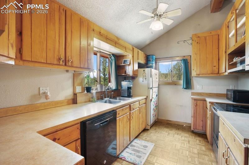 Kitchen featuring black appliances, vaulted ceiling, light countertops, plenty of natural light, and a textured ceiling