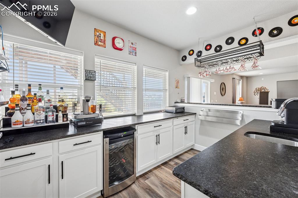Basement wet bar/kitchen has a wine cooler, white cabinets, easy care wood-style flooring, recessed lighting, and granite countertops.  Even has a passthrough window to the outside patio for a perfect summer BBQ.