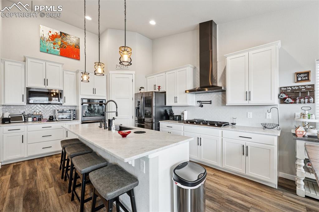Large gourmet kitchen showcasing beautiful white cabinetry, a breakfast bar area, marble counters, hanging light fixtures, and high-end appliances.