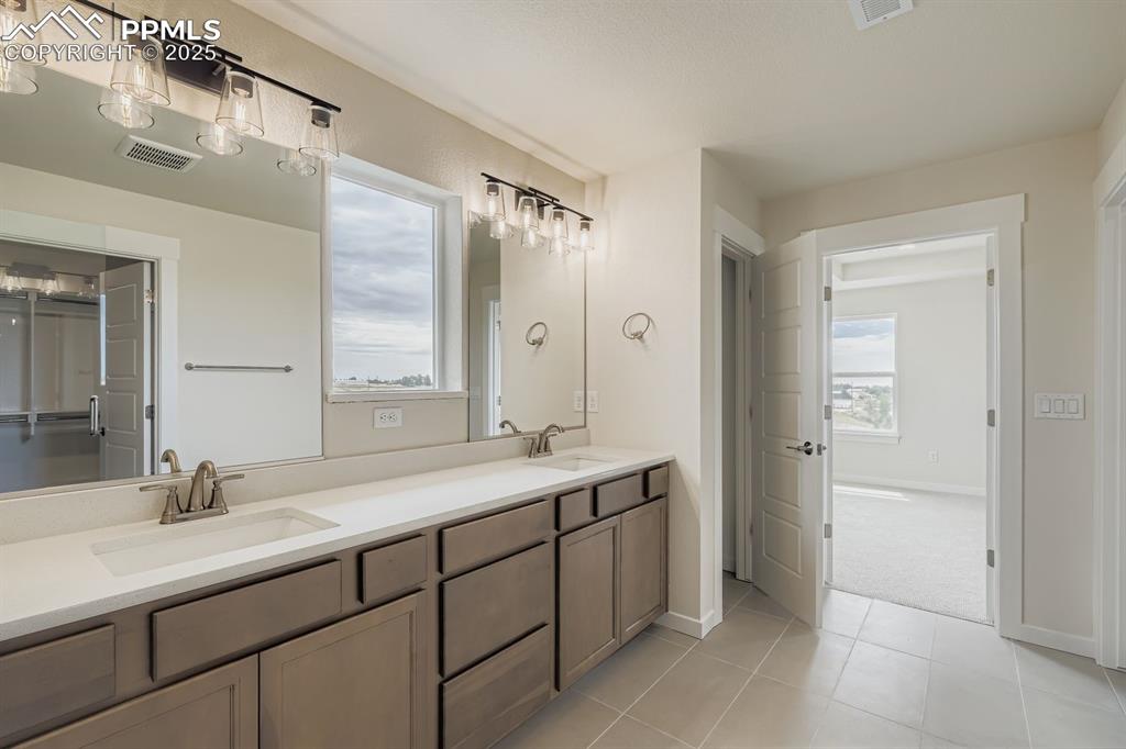 Bathroom with double vanity, light tile patterned floors, and a closet