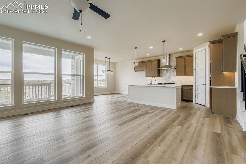 Kitchen featuring an island with sink, hanging light fixtures, open floor plan, tasteful backsplash, and light wood finished floors