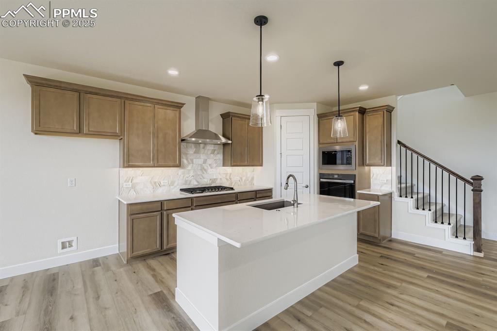 Kitchen featuring decorative backsplash, brown cabinetry, hanging light fixtures, an island with sink, and recessed lighting