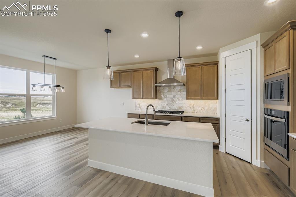 Kitchen featuring pendant lighting, decorative backsplash, a kitchen island with sink, light stone counters, and appliances with stainless steel finishes