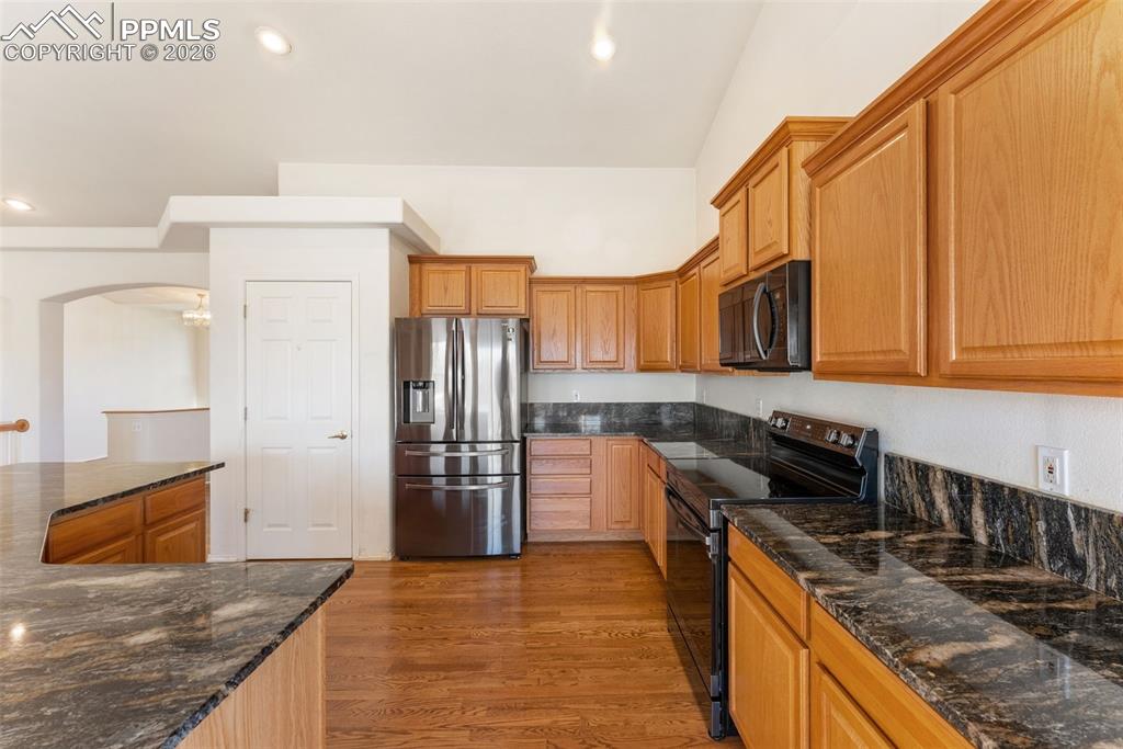 Kitchen featuring black appliances, dark stone countertops, light wood-style floors, arched walkways, and recessed lighting