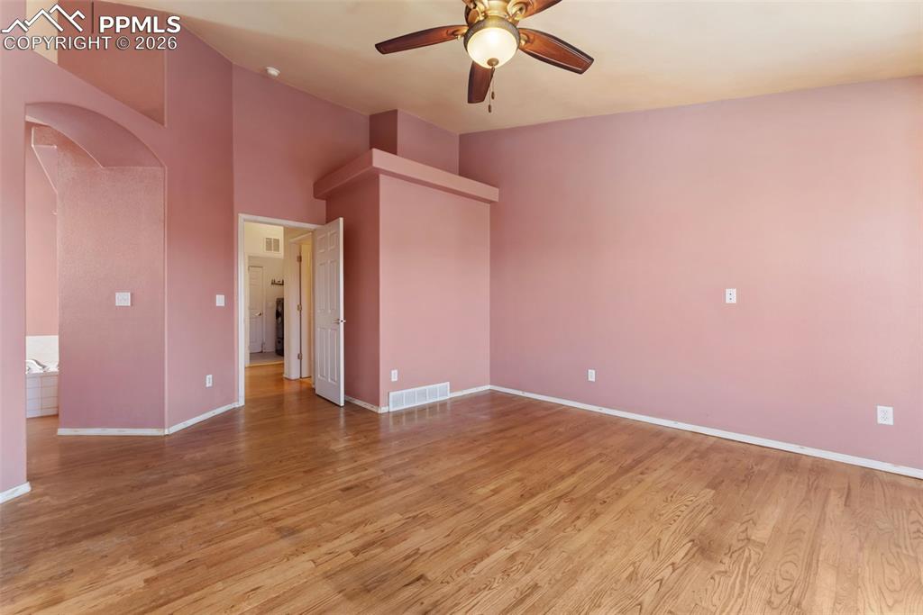 Empty room with arched walkways, light wood-style floors, a ceiling fan, and a towering ceiling
