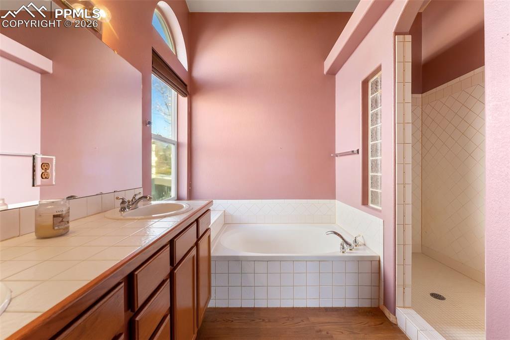 Full bath featuring a shower stall, a garden tub, wood finished floors, and double vanity