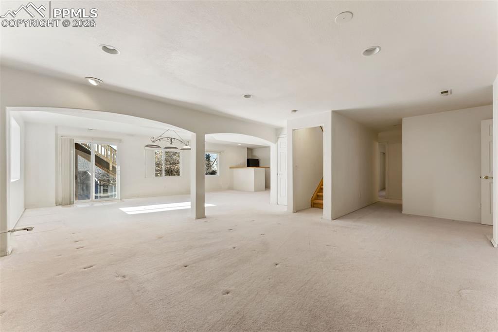 Unfurnished living room featuring arched walkways, stairs, and carpet