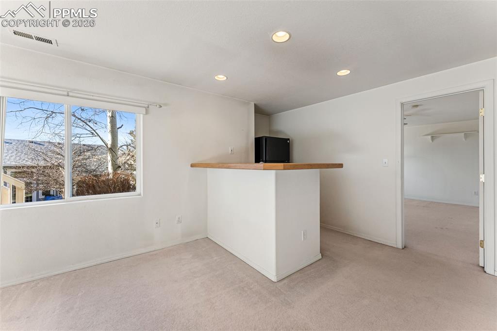 Bar with light carpet, wooden counters, freestanding refrigerator, and recessed lighting