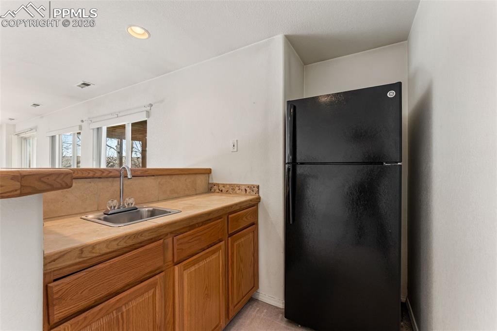 Kitchen with freestanding refrigerator, brown cabinetry, tile countertops, and recessed lighting