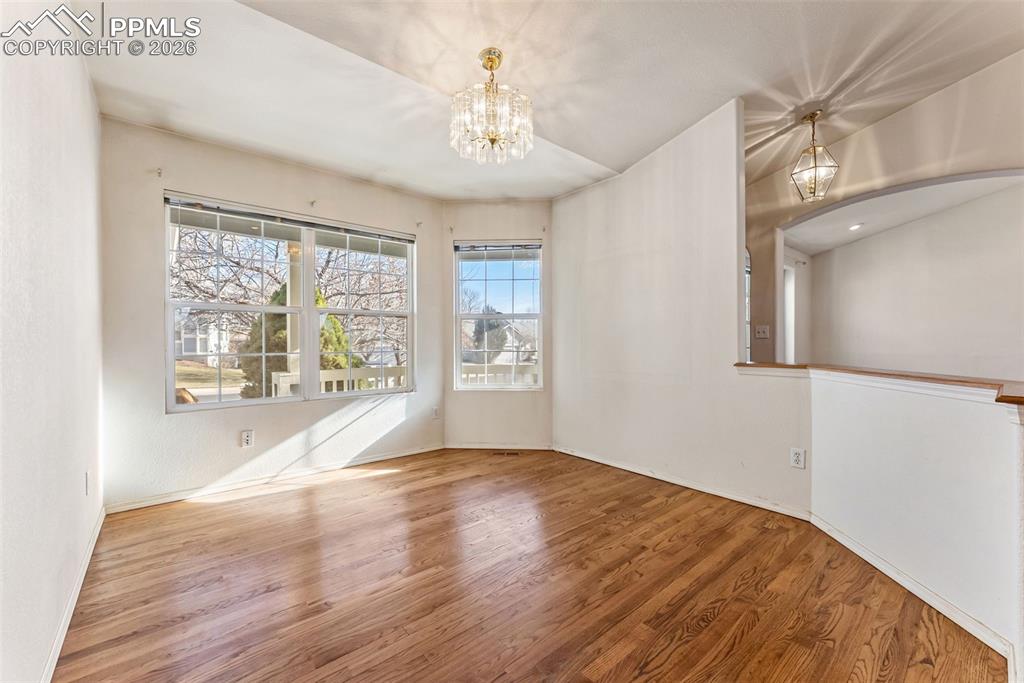 Spare room featuring wood finished floors, a chandelier, and vaulted ceiling