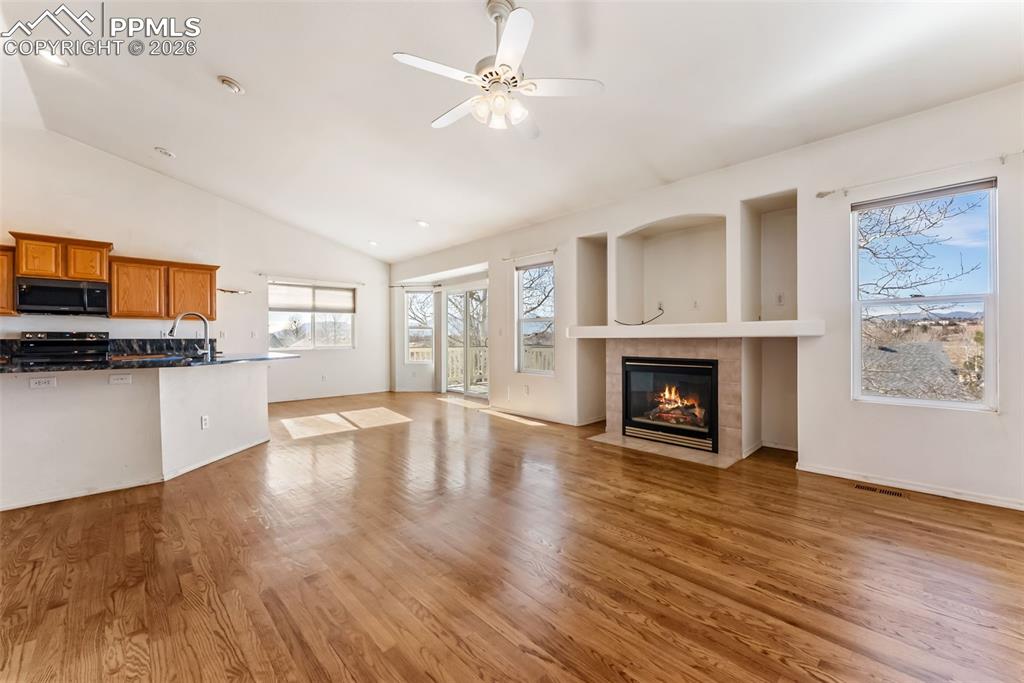 Unfurnished living room featuring a fireplace, a ceiling fan, light wood-style floors, and high vaulted ceiling