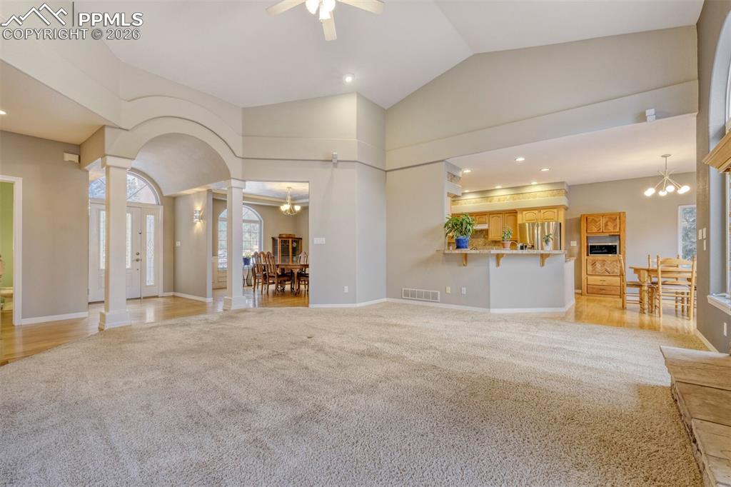 living room with suspended lighting, light colored carpet, ornate columns, lofted ceiling, and a ceiling fan