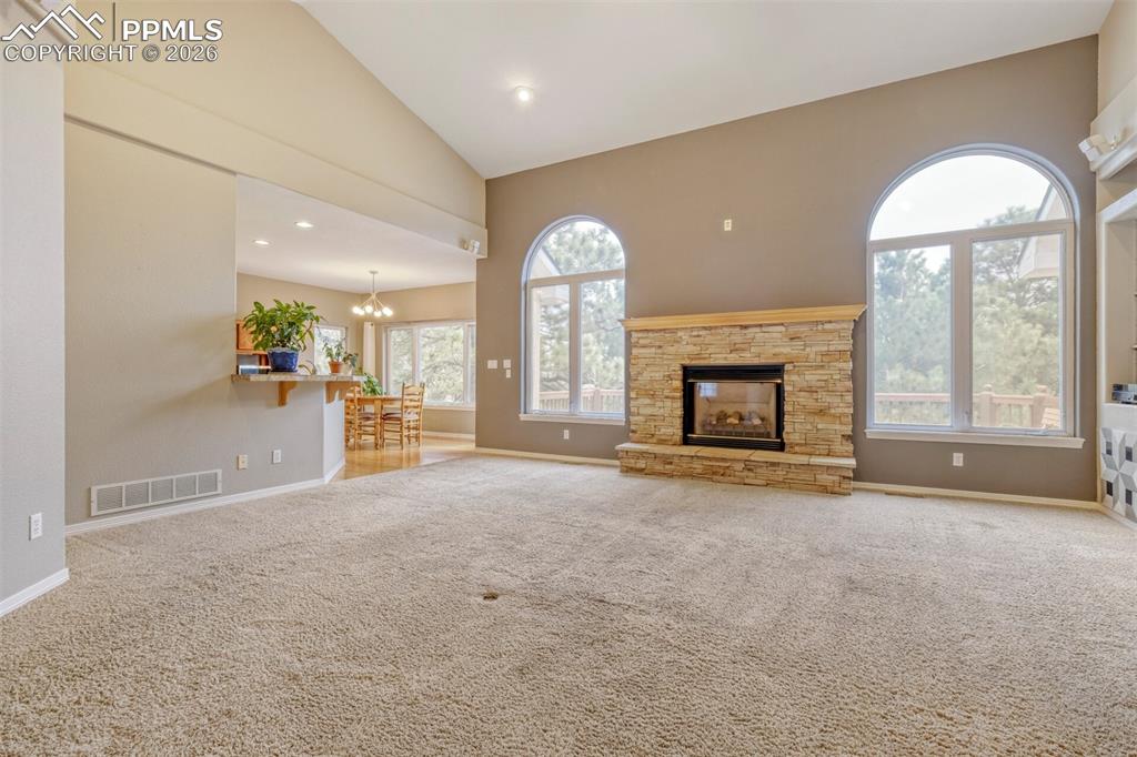  living room featuring a fireplace, light colored carpet, vaulted ceiling, and hanging lights