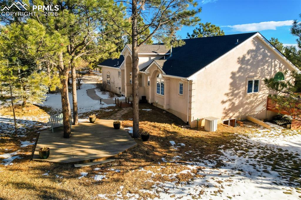 Snow covered property with stucco siding, a shingled roof, a wooden deck, and a patio