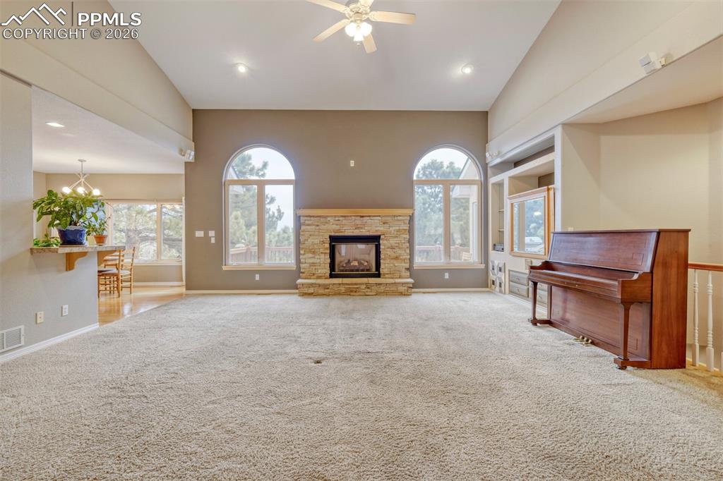 living room with a stone fireplace, carpet flooring, ceiling fan, and hanging lights