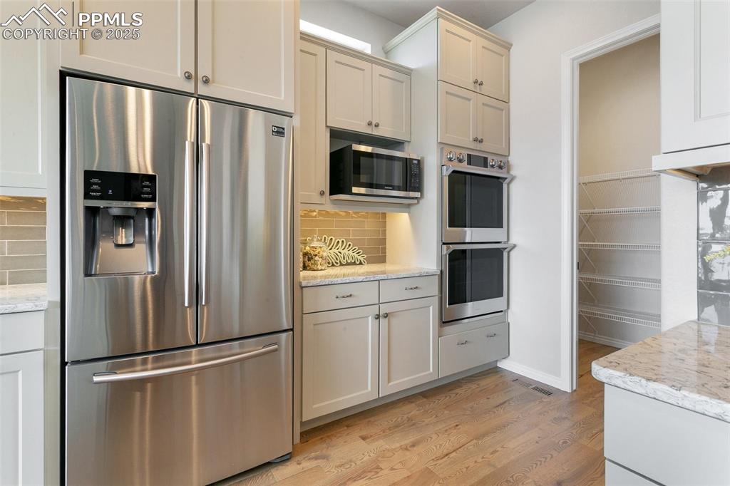 Kitchen with stainless steel appliances, light wood-style flooring, backsplash, and light stone countertops