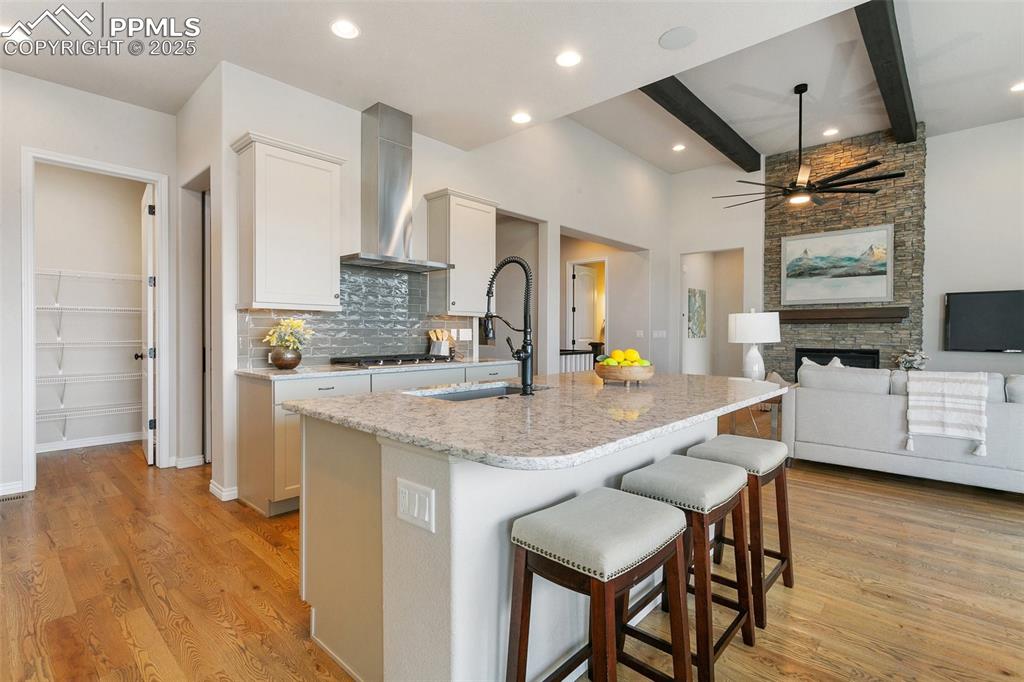 Kitchen with wall chimney exhaust hood, tasteful backsplash, beamed ceiling, light wood-style floors, and stainless steel gas stovetop