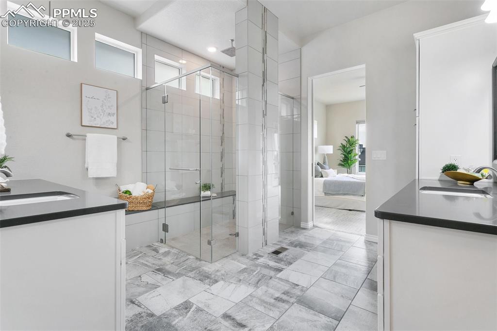 Bathroom featuring double vanity, a stall shower, ensuite bathroom, and marble look tiles