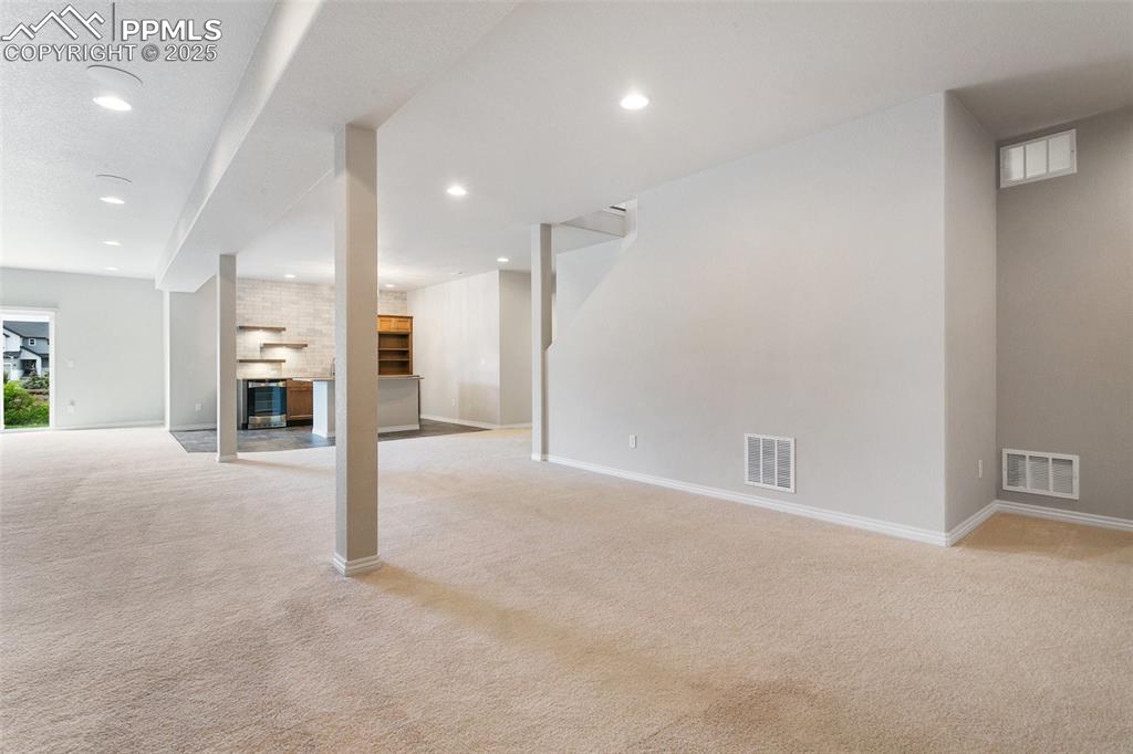 Unfurnished living room with light carpet, a brick fireplace, beverage cooler, and recessed lighting