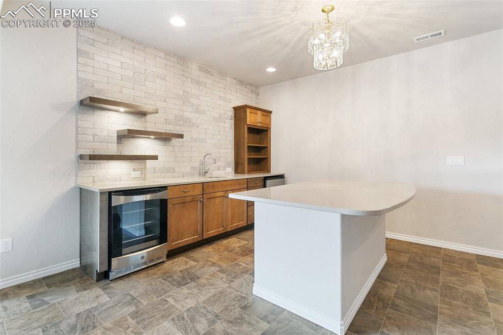 Kitchen featuring beverage cooler, open shelves, brown cabinetry, light countertops, and a chandelier