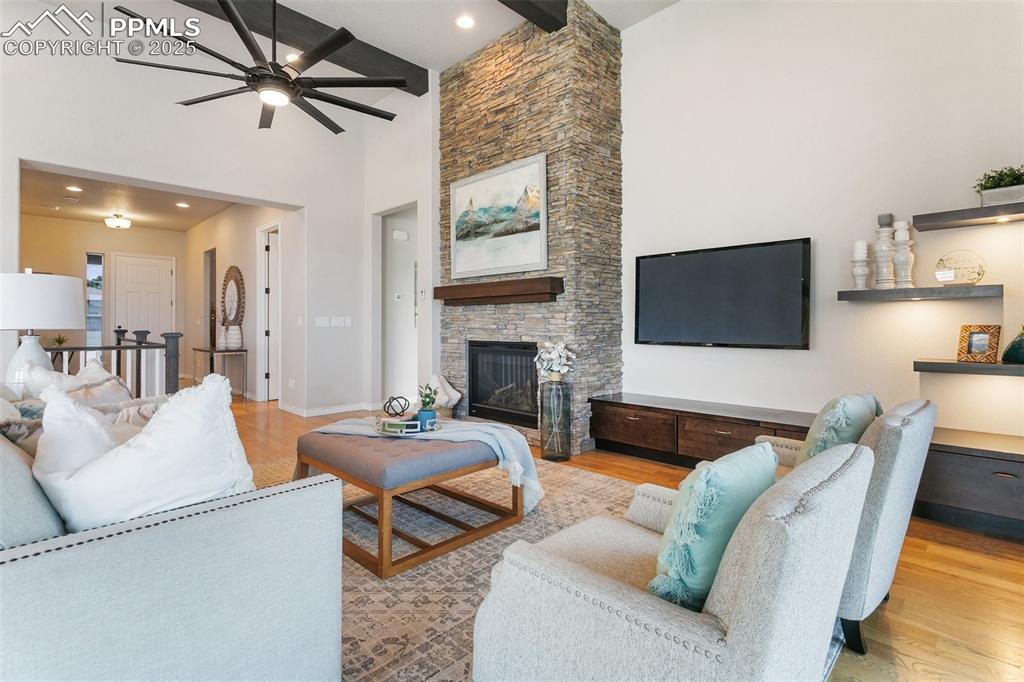 Living area featuring ceiling fan, high vaulted ceiling, beam ceiling, wood finished floors, and a stone fireplace