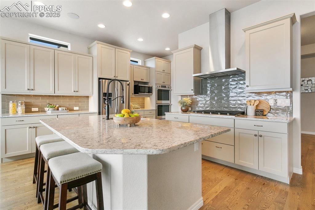 Kitchen featuring wall chimney exhaust hood, stainless steel appliances, tasteful backsplash, a breakfast bar area, and a kitchen island with sink