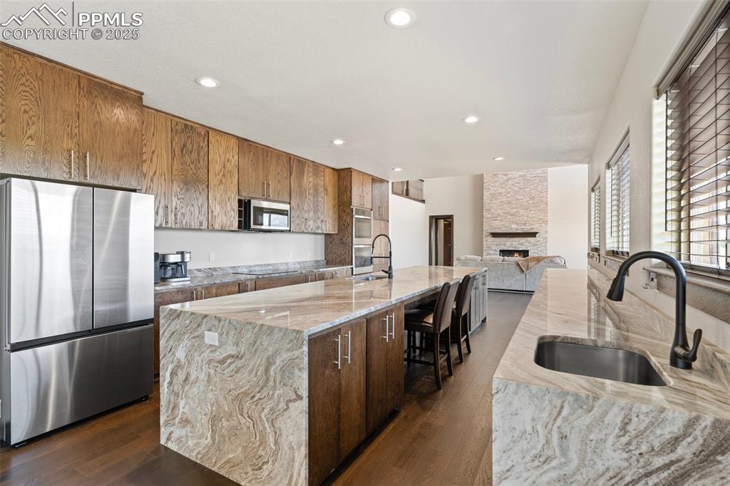 Kitchen featuring stainless steel appliances, light stone counters, dark wood flooring, a stone fireplace, and recessed lighting
