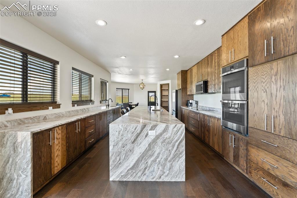 Kitchen with stainless steel appliances, dark wood finished floors, recessed lighting, a center island with sink, and light stone countertops