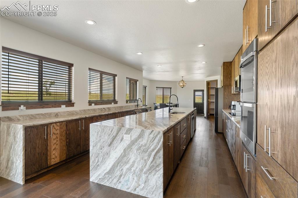 Kitchen featuring a waterfall island with sink, dark wood flooring, recessed lighting, light stone counters, and double oven