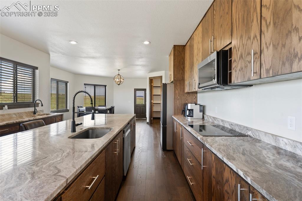 Kitchen with appliances with stainless steel finishes, dark wood flooring, eat-in kitchen, light stone countertops, and recessed lighting