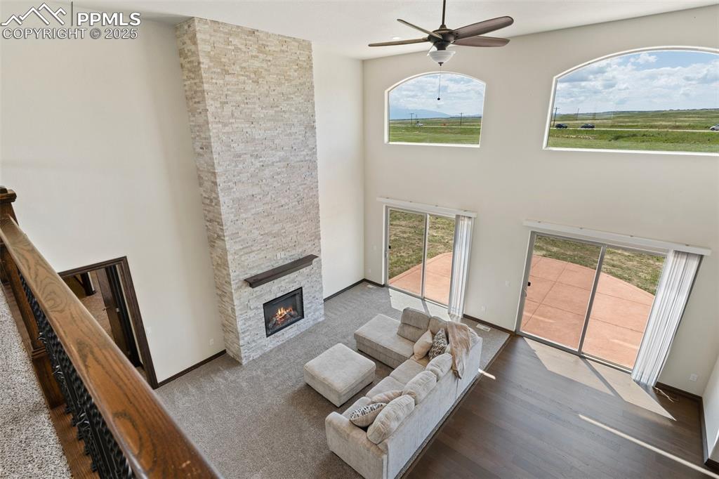 Living room from loft with plenty of natural light, a fireplace, a ceiling fan, a towering ceiling, and wood finished floors