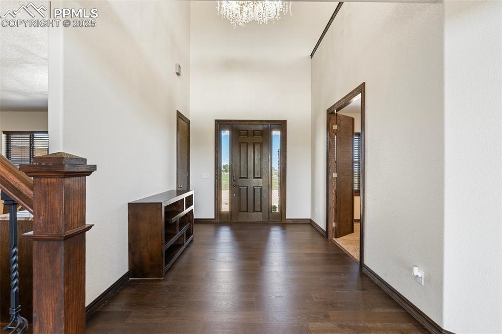 Foyer with dark wood floors, a chandelier, a towering ceiling, and stairs