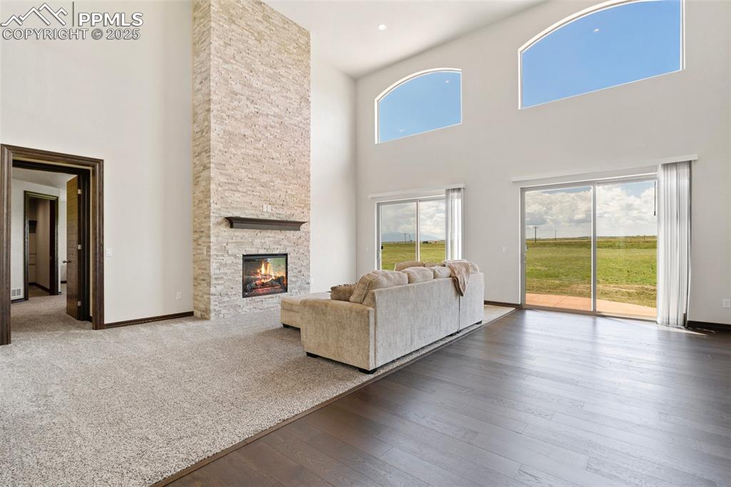 Living room featuring a towering ceiling, a stone fireplace, and wood and carpet flooring