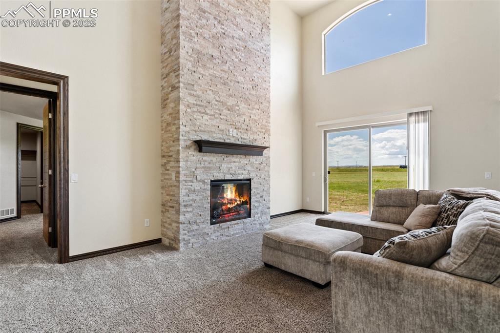 Carpeted living area with a towering ceiling and a stone fireplace
