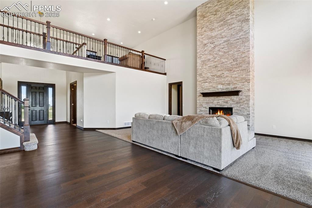 Living room featuring stairs, a towering ceiling, wood finished floors, a stone fireplace, and recessed lighting