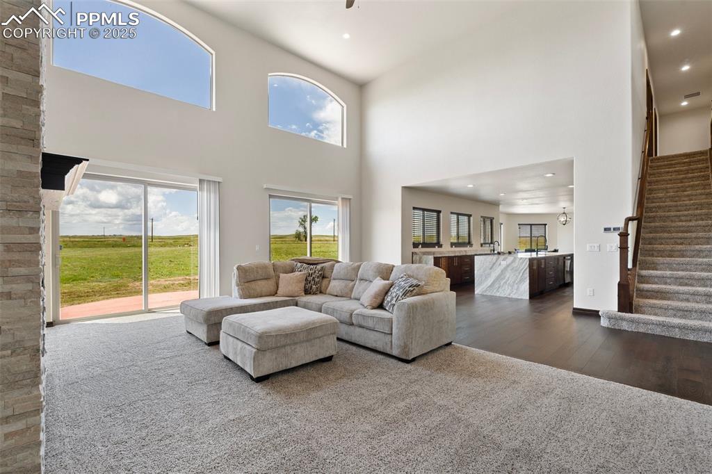 Living area with wood finished floors, stairs, a towering ceiling, and recessed lighting