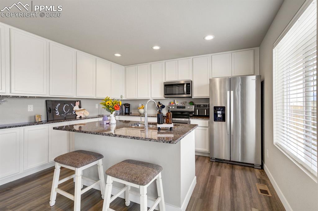 Kitchen featuring appliances with stainless steel finishes, dark stone counters, white cabinetry, a center island with sink, and a breakfast bar