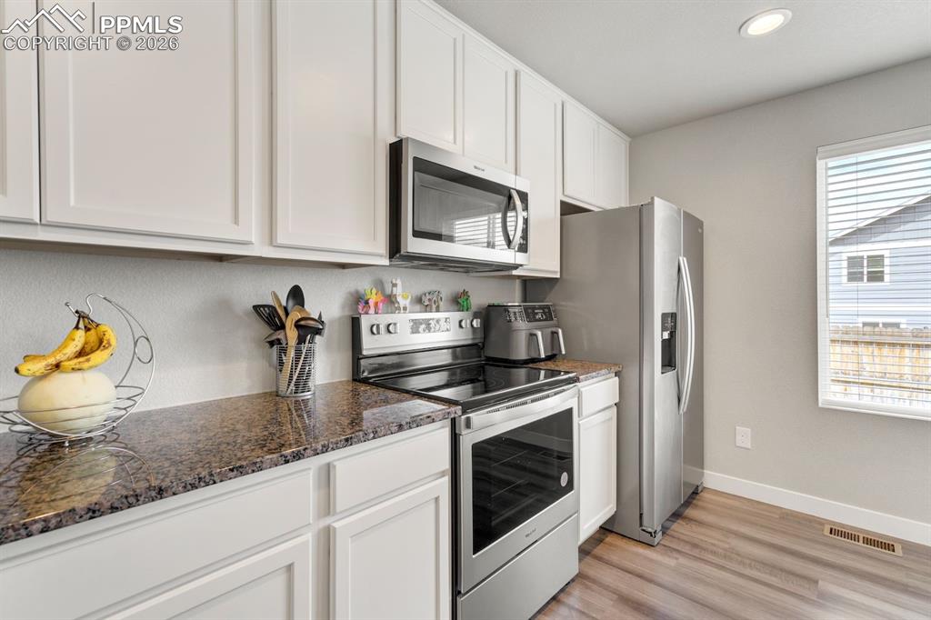 Kitchen featuring appliances with stainless steel finishes, white cabinets, dark stone counters, light wood-type flooring, and recessed lighting
