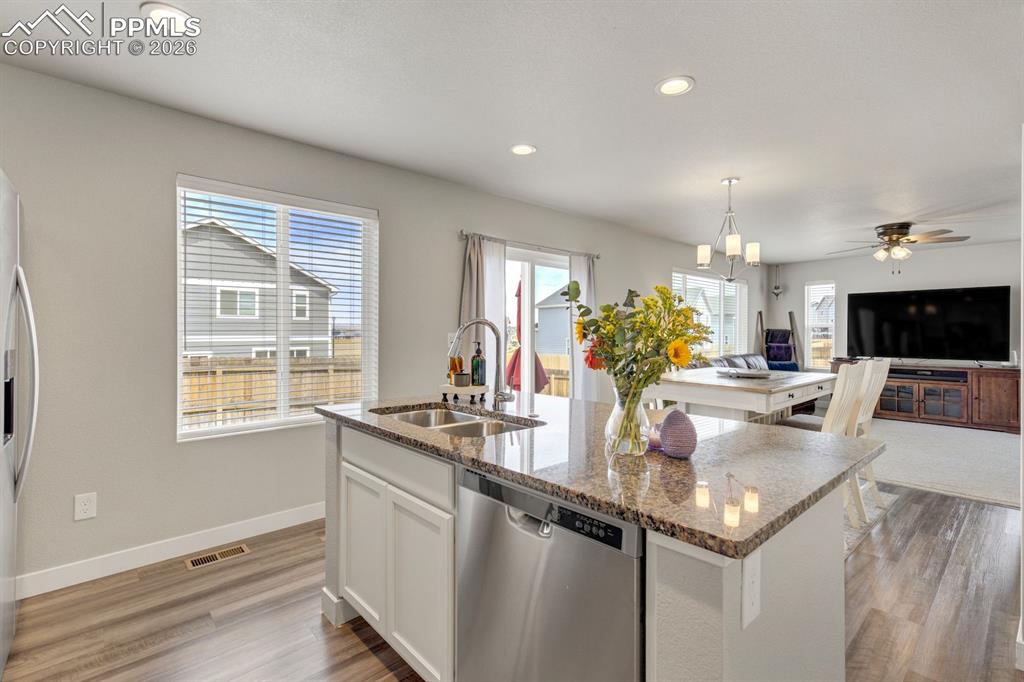 Kitchen with white cabinets, appliances with stainless steel finishes, dark stone counters, ceiling fan, and a kitchen island with sink