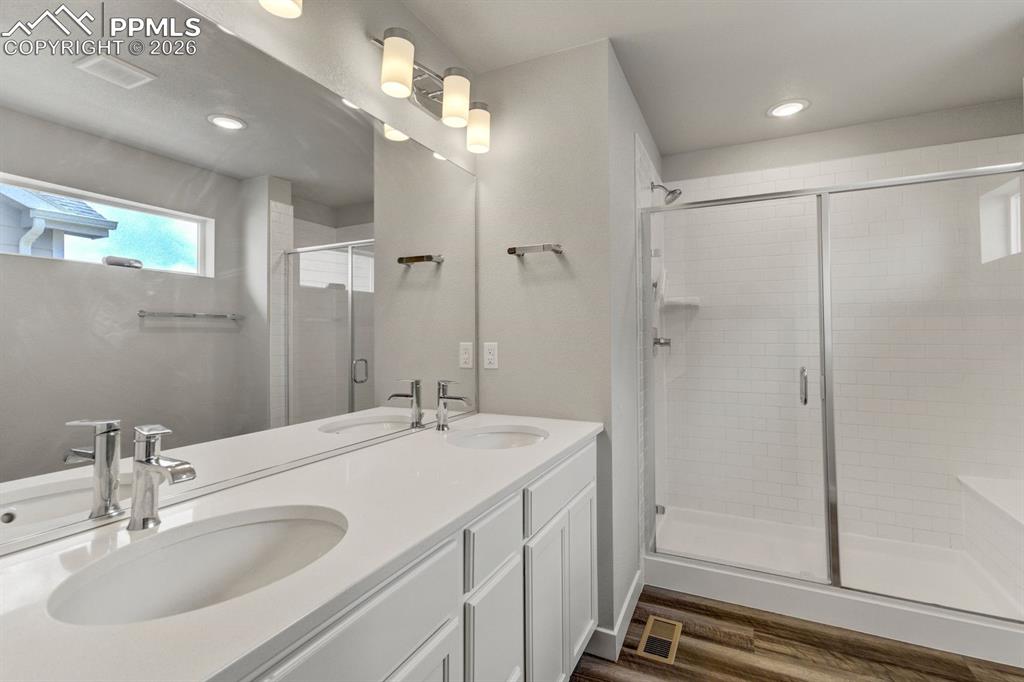 Bathroom with double vanity, dark wood-type flooring, a shower stall, and recessed lighting