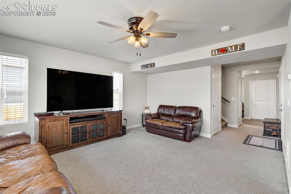 Living area with light colored carpet, ceiling fan, plenty of natural light, and stairs