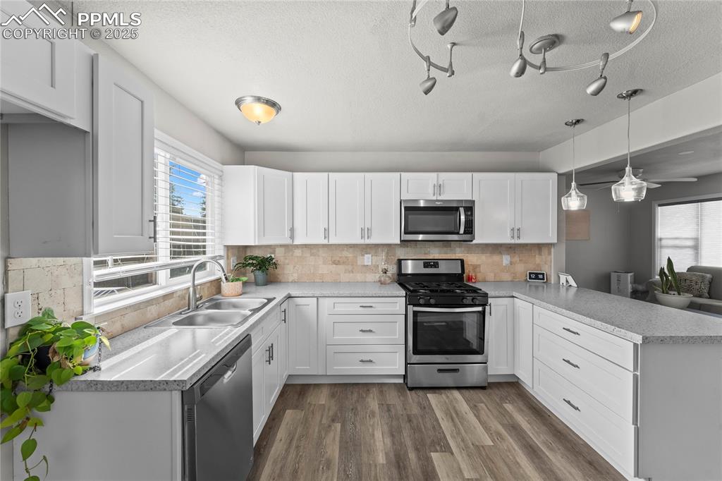 Kitchen featuring stainless steel appliances, dark wood-style floors, a peninsula, white cabinets, and a textured ceiling