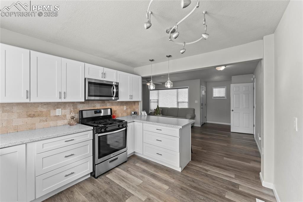 Kitchen with white cabinets, stainless steel appliances, decorative backsplash, hanging light fixtures, and a textured ceiling