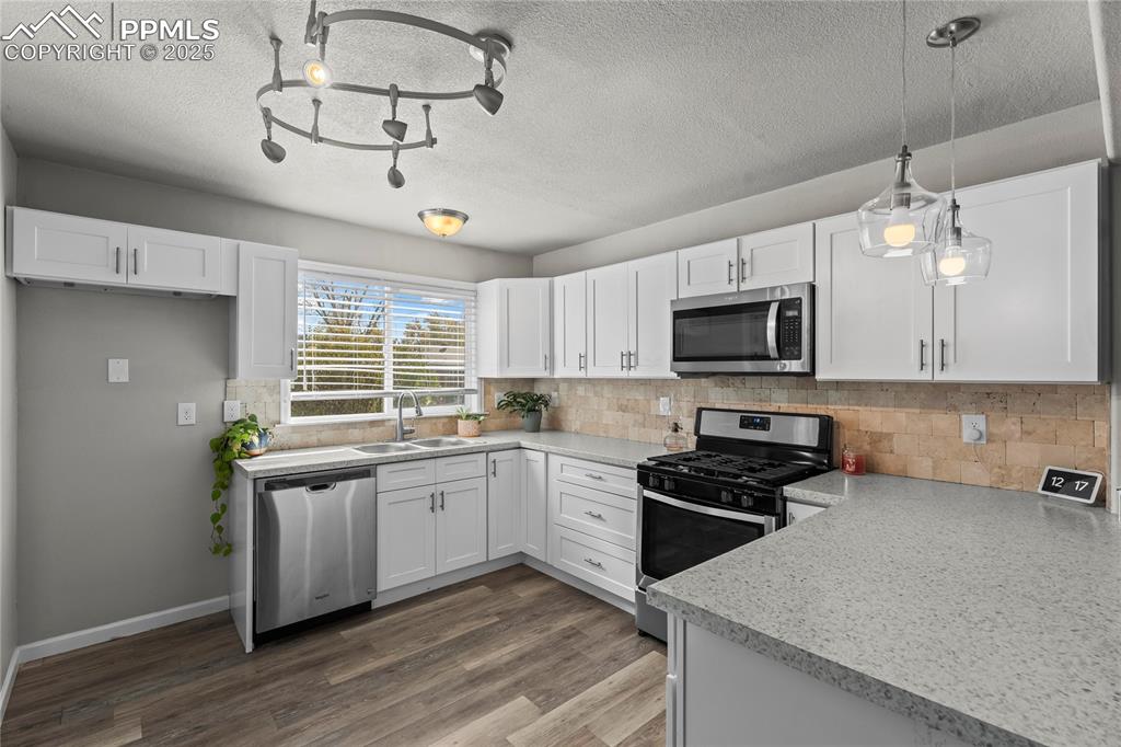 Kitchen with stainless steel appliances, white cabinets, light countertops, backsplash, and a textured ceiling