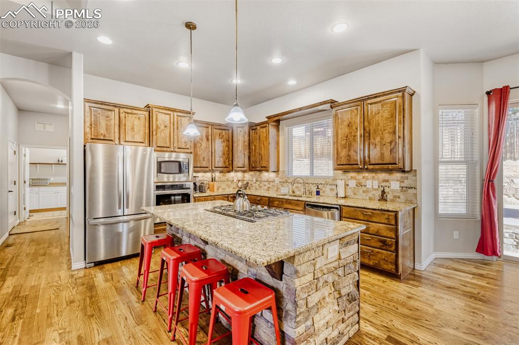 Gourmet kitchen with stainless steel appliances, pendant lighting, hardwood flooring, knotty pine cabinetry and a kitchen island
