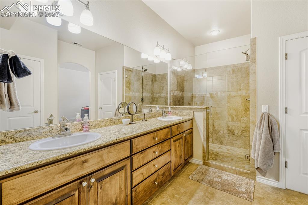 Junior basement ensuite bath featuring a shower stall, double vanity, and Travertine tile flooring
