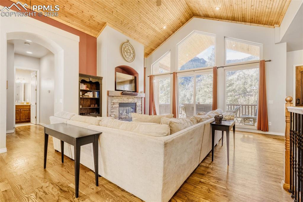 Living area featuring a high wooden ceiling, healthy amount of natural light, a stone fireplace, and arched walkways. Covered front deck with mountain views is a plus