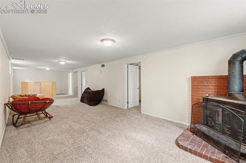 Living room with a wood stove, ornamental molding, light carpet, and a textured ceiling
