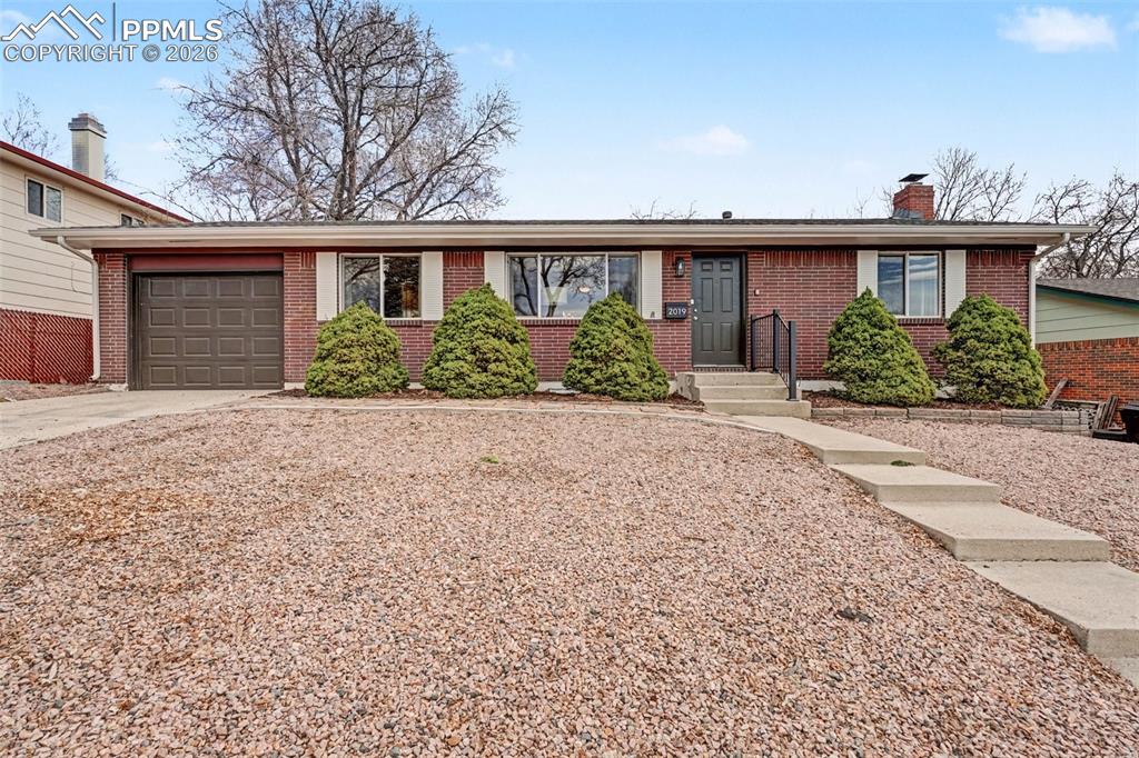 Single story home with a garage, brick siding, concrete driveway, and a chimney
